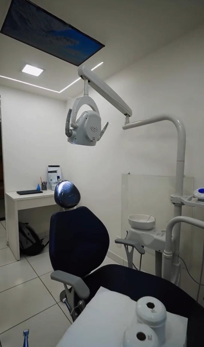 Sala de atendimento com cadeira odontológica azul e luminária